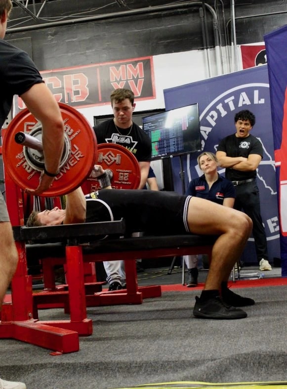 A Forte Strength athlete pressing a bench attempt at a meet with spotters either side