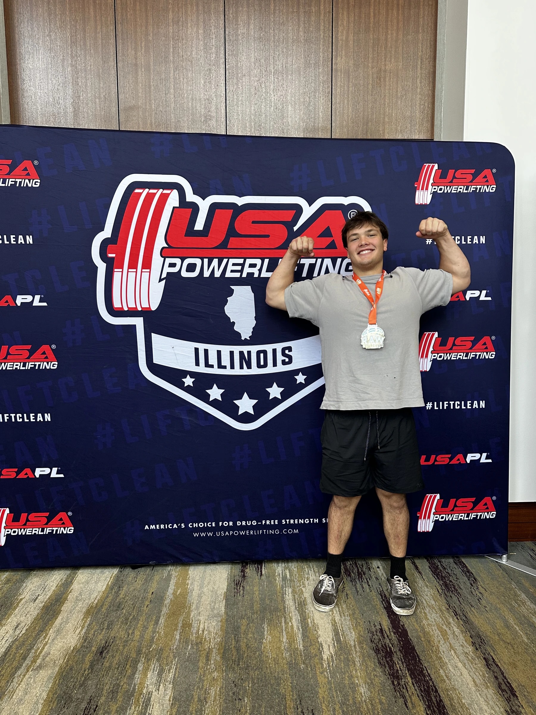 A Forte Strength athlete flexing with a medal in front of a USA Powerlifting backdrop