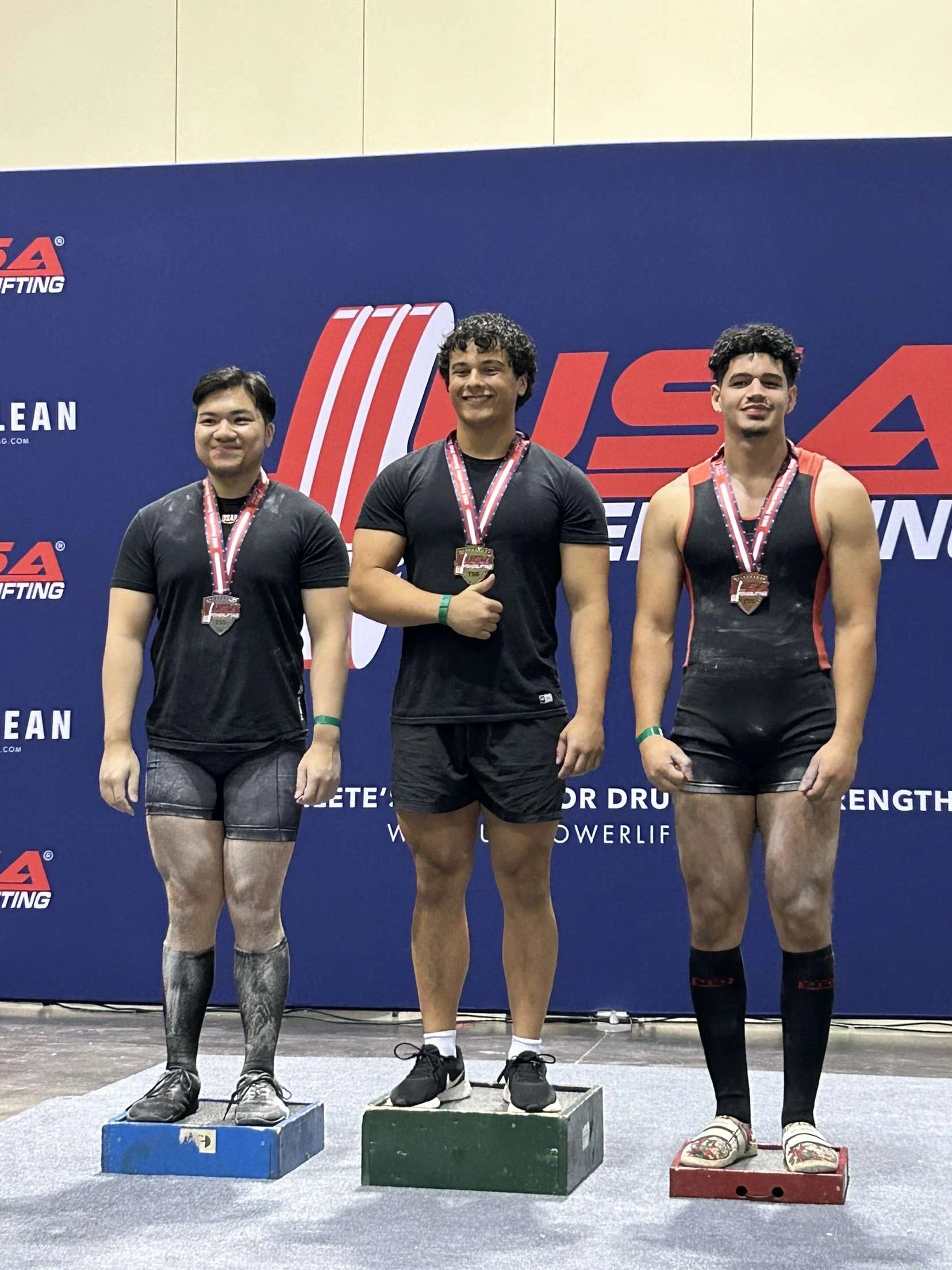 Three Forte Strength athletes standing on the podium with their medals at a USA Powerlifting meet