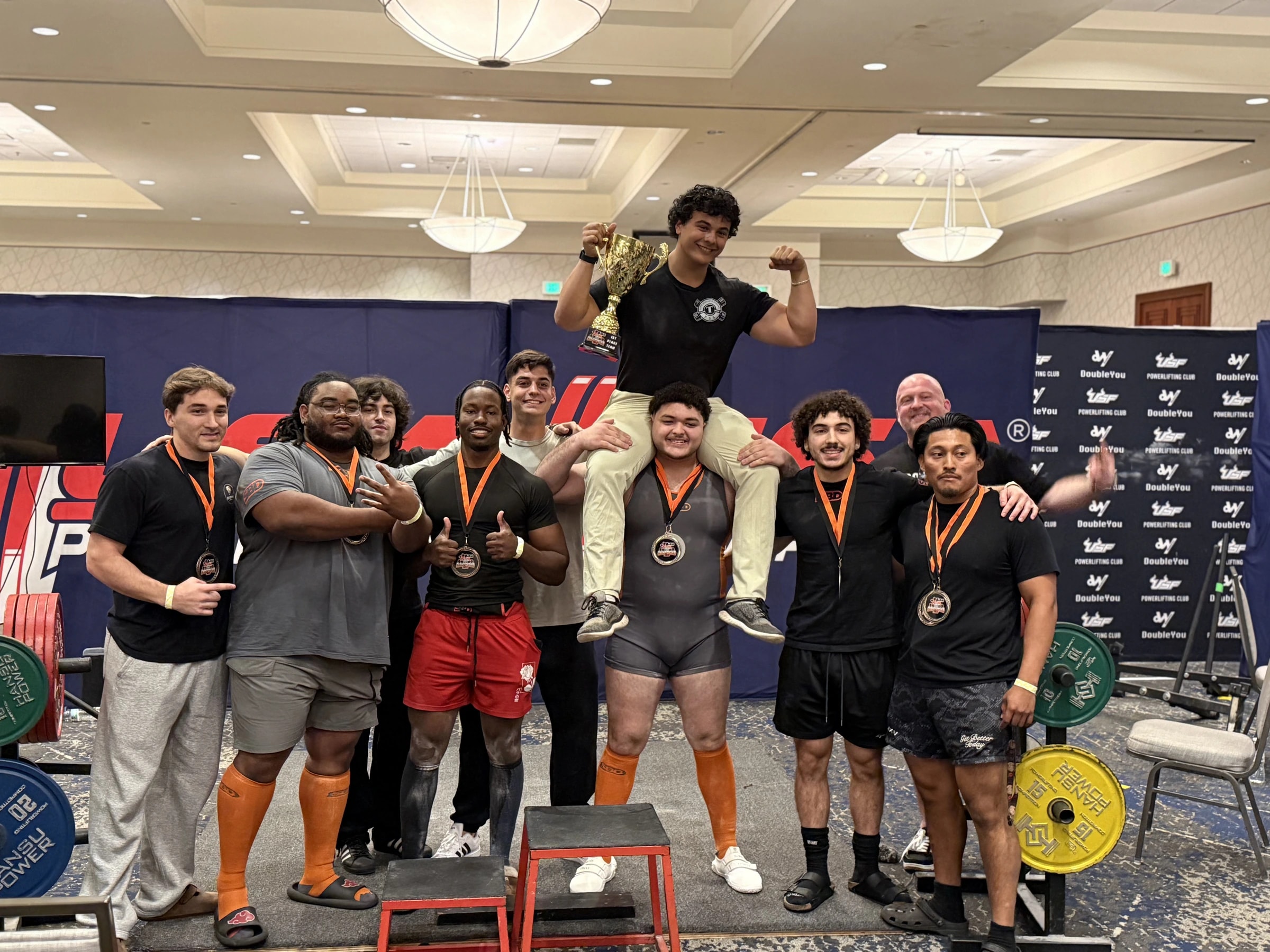 The Forte Strength team together in the venue after a meet, medals around their necks and the team trophy held up