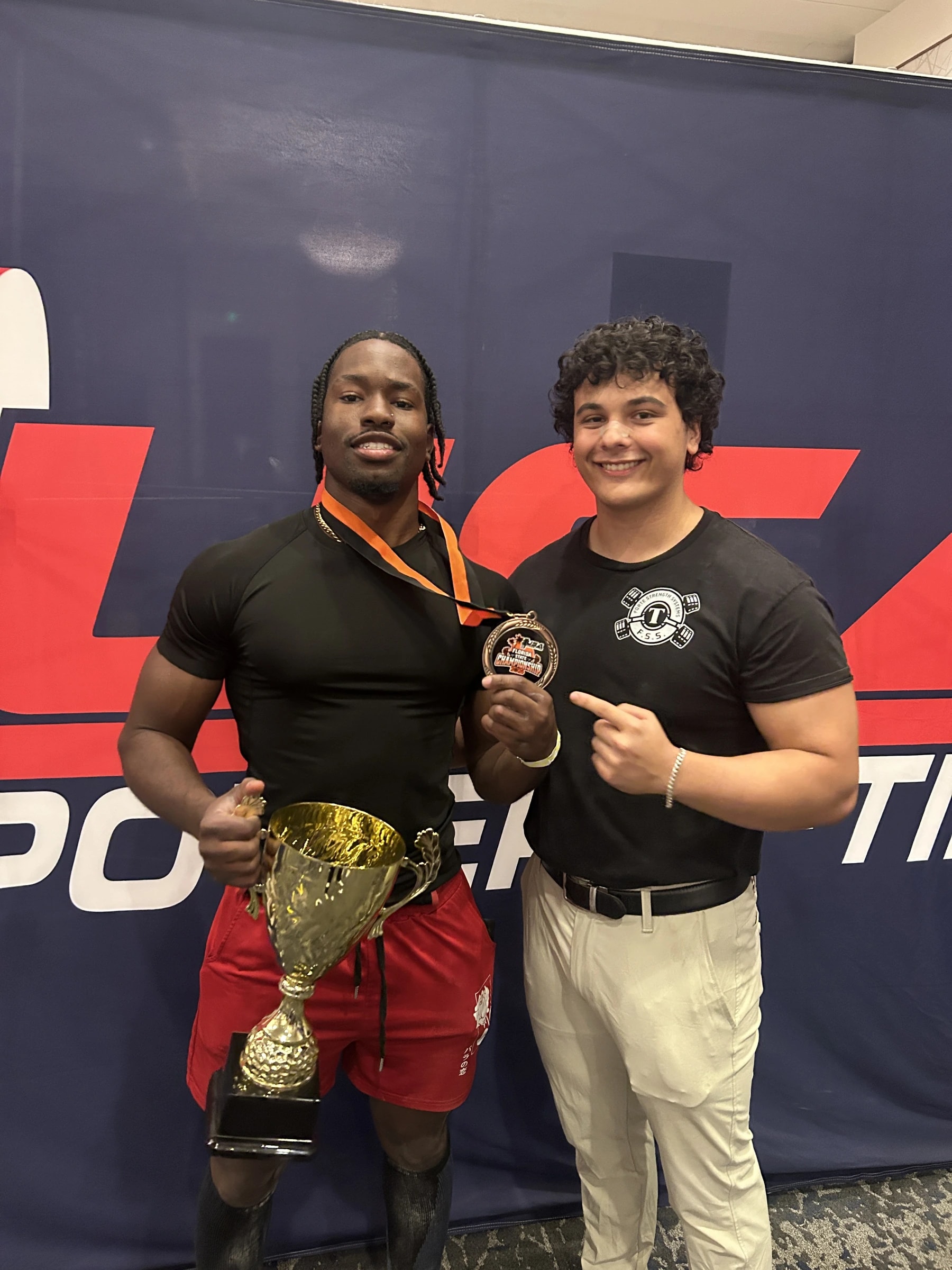Two Forte Strength athletes with a first-place team trophy and a medal at a USA Powerlifting meet