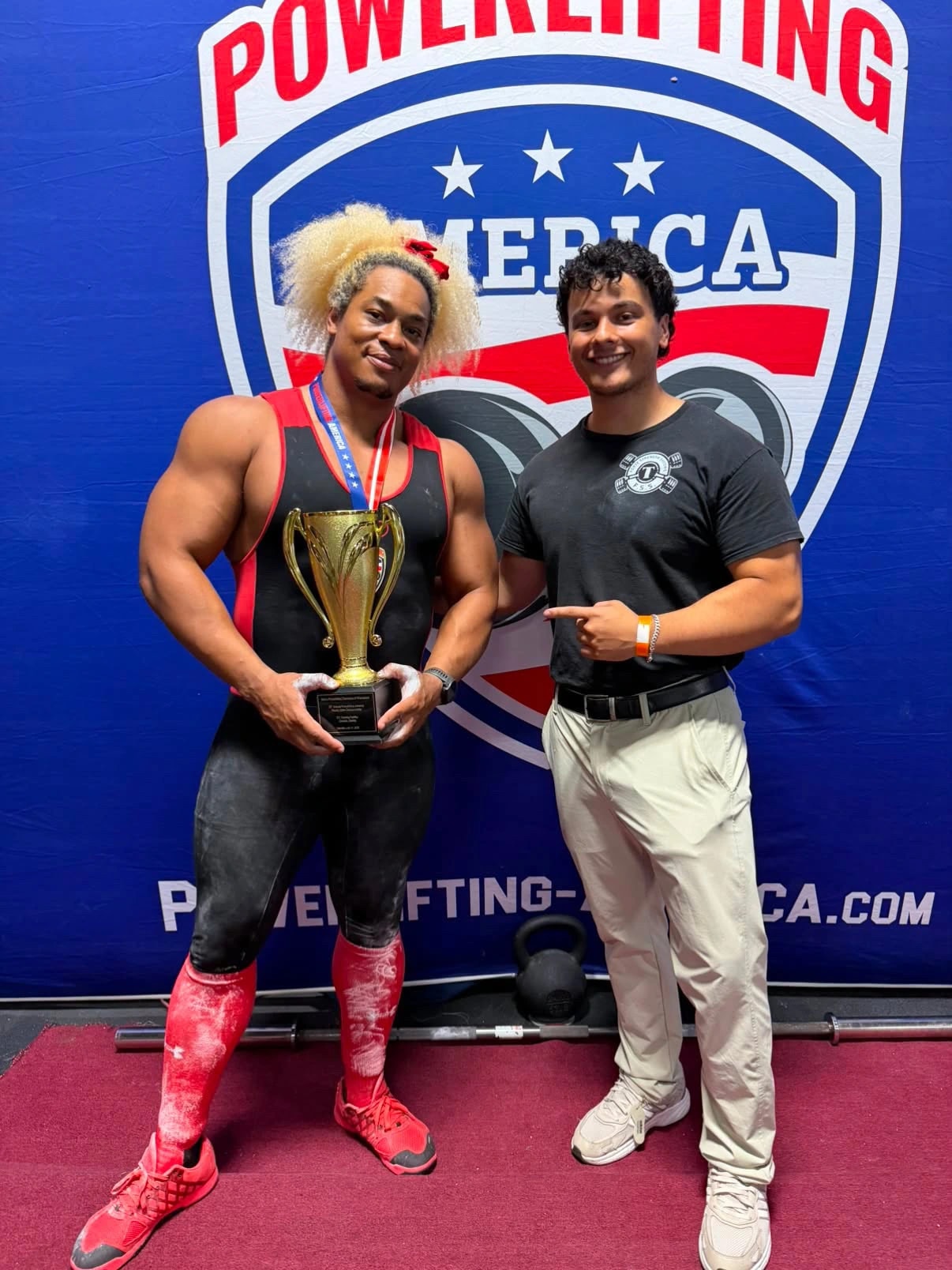 Two Forte Strength lifters with a trophy in front of a Powerlifting America backdrop
